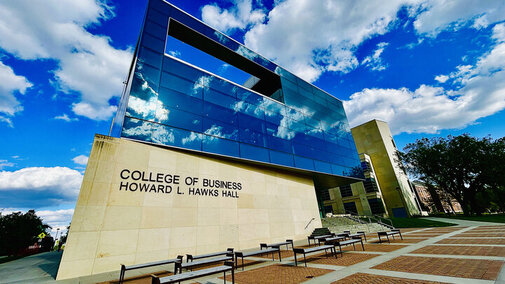 Howard L. Hawks Hall's modern glass facade against a vibrant blue sky trimmed with clouds.